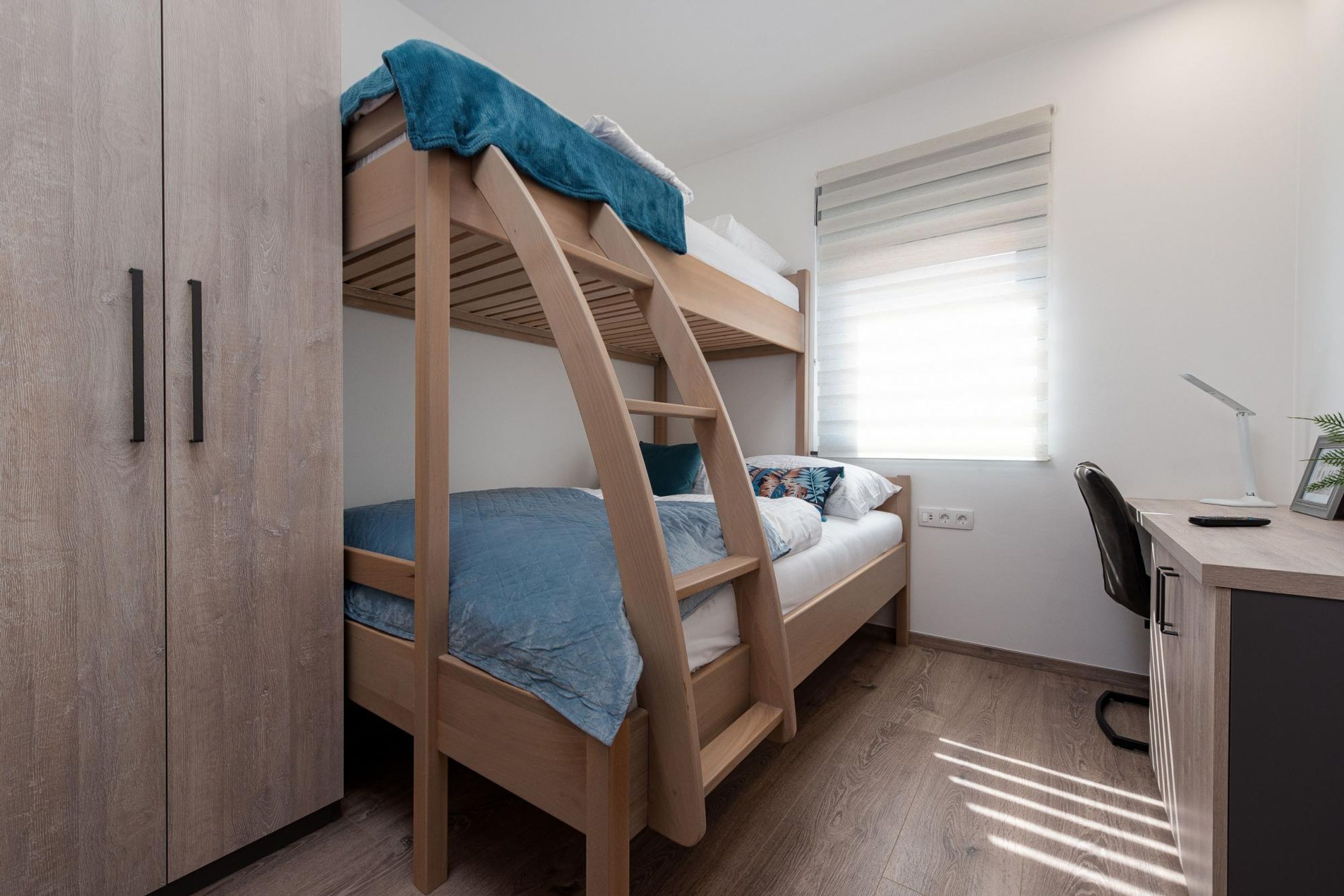 Una cama en literas con escritorio y silla, un armario y una ventana con persianas.