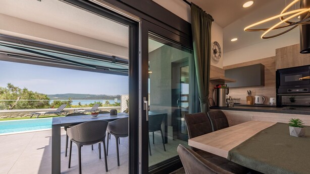 A modern kitchen with a built-in oven and a dining area with a glass door leading to a balcony with a pool view.