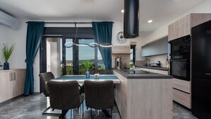 A modern kitchen with a central island, dark curtains, and a view to the outdoors.