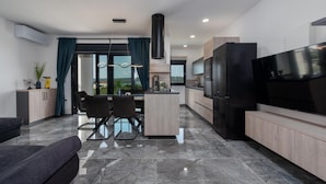 A modern kitchen with a large TV, a dining area with a glass table, and a view of the outdoors.