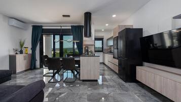 A modern kitchen with a large TV, a dining area with a glass table, and a view of the outdoors.