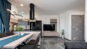 A modern living room with a dining area, a kitchen, and a TV mounted on the wall.