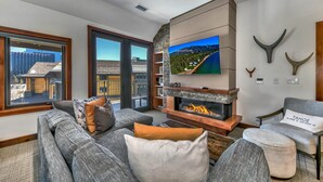 A modern living room with a fireplace, a large TV, and a view of the city through large windows.