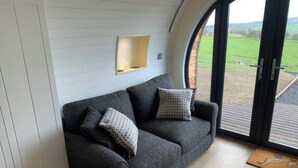 Een grijze bank met gekleurde kussens in een kamer met een witte muur en een groot raam.