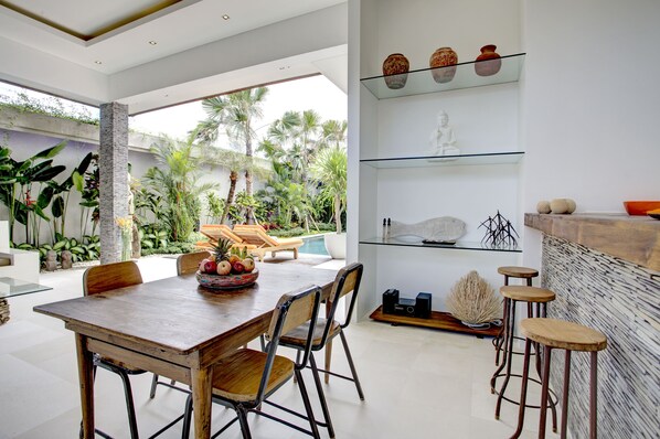 Un espace repas moderne avec une table en bois, des chaises et une vue sur une piscine et un jardin.