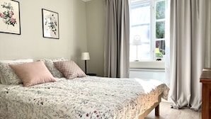 Un dormitorio con colcha estampada, lámpara de noche y ventana con cortinas.
