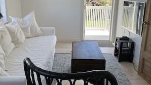 Una sala de estar moderna con un sofá blanco, un sillón de mimbre negro, una mesa de centro de madera y un televisor sobre un soporte.