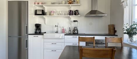 A modern kitchen with white cabinetry, a stainless steel refrigerator, a wooden dining table with chairs, and a window with a view.