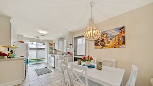 A modern kitchen with white cabinetry, a dining area with a white table and chairs, a chandelier, and a painting on the wall. - Mykonos: Beautifully updated with heated pool, moments to the Gulf (Anna Maria)