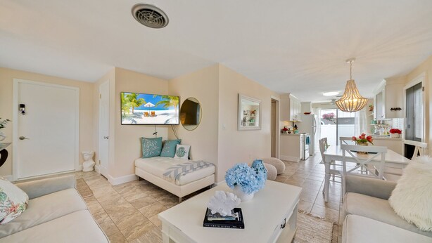A spacious living room with a white sofa, a coffee table with decorative items, and a television mounted on the wall. - Mykonos: Beautifully updated with heated pool, moments to the Gulf (Anna Maria)