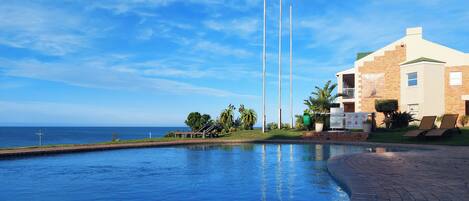 A swimming pool with a curved edge, a building with a brick facade, and a clear blue sky.
