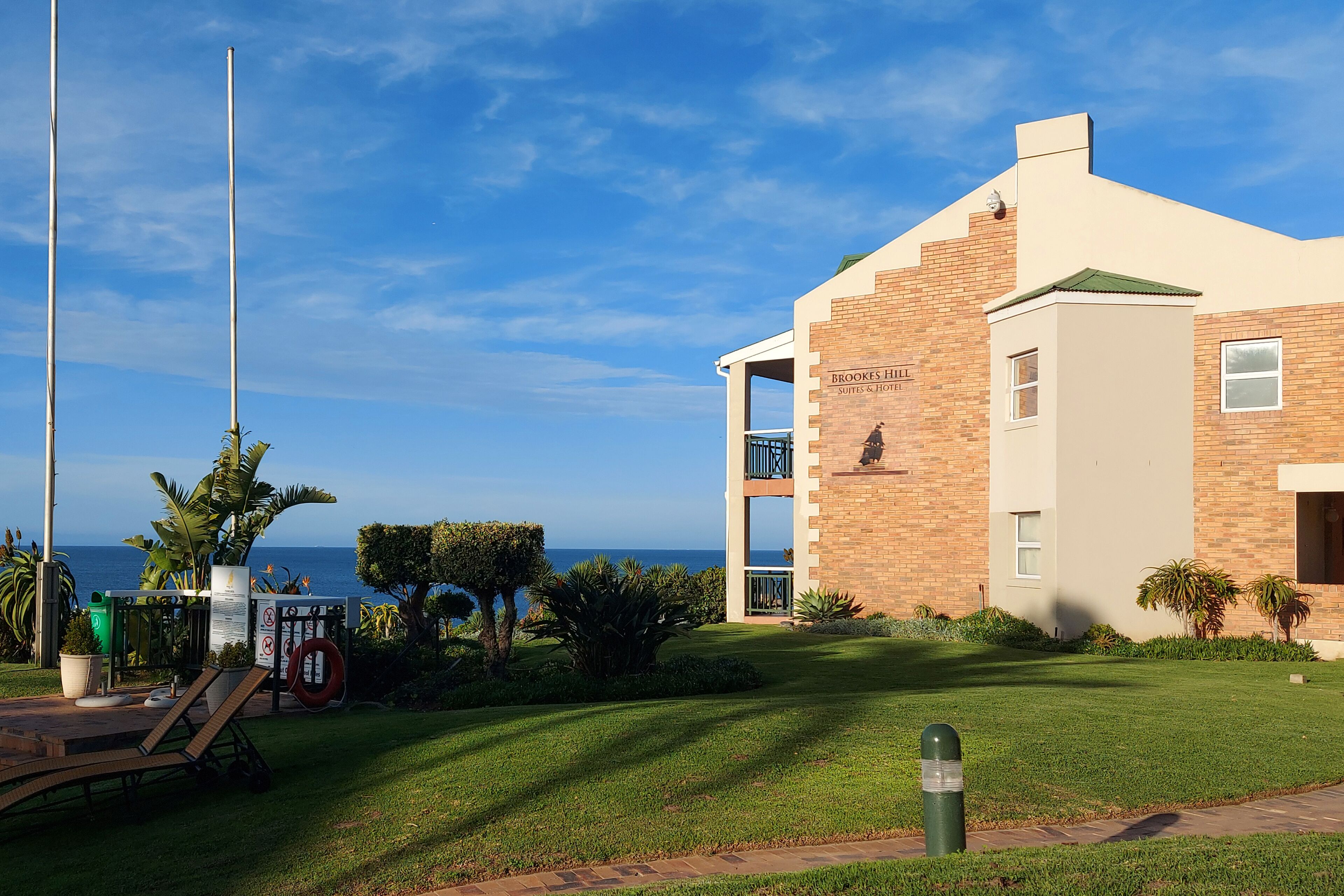Un edifici modern amb un rètol que diu "Brookes Hill Suites & Hotel", un jardí ben cuidat i una vista despejada de l'oceà.
