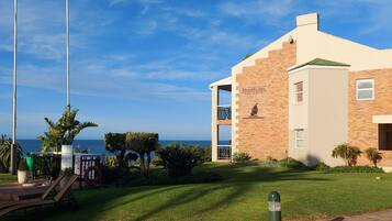 Un edifici modern amb un rètol que diu "Brookes Hill Suites & Hotel", un jardí ben cuidat i una vista despejada de l'oceà.