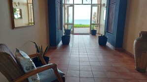 Un pasillo con vista al océano, plantas en macetas y una silla de mimbre.