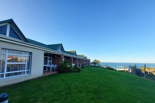 Un hotel con césped, un patio con sillas y vista al océano.