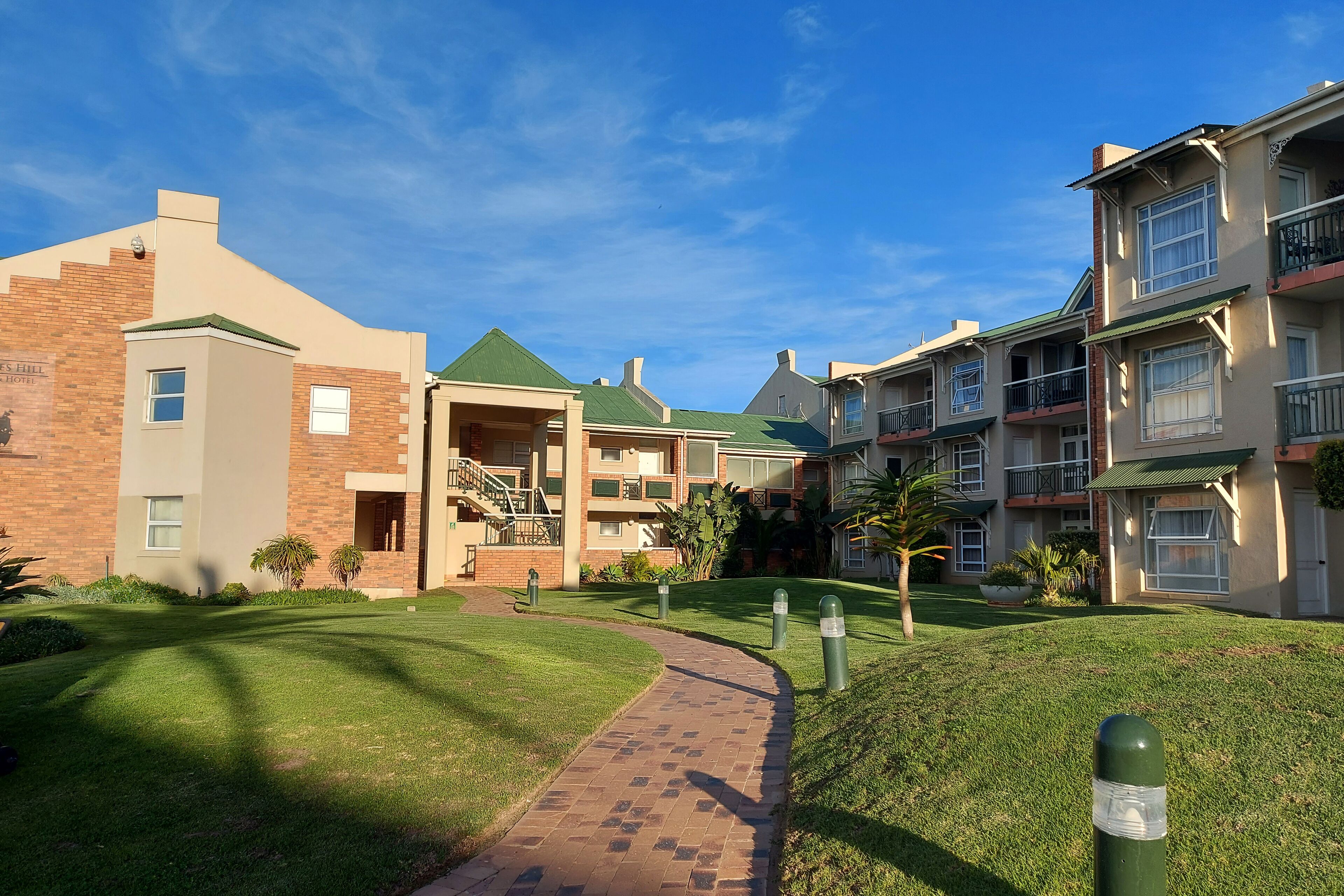 A residential building with a brick facade, a green roof, and a pathway leading to a gated entrance.