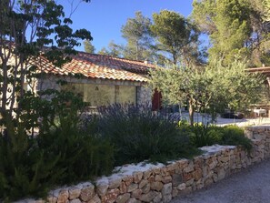 Un bâtiment rustique en pierre, doté d’un toit en tuiles, entouré d’une végétation luxuriante et d’arbres.