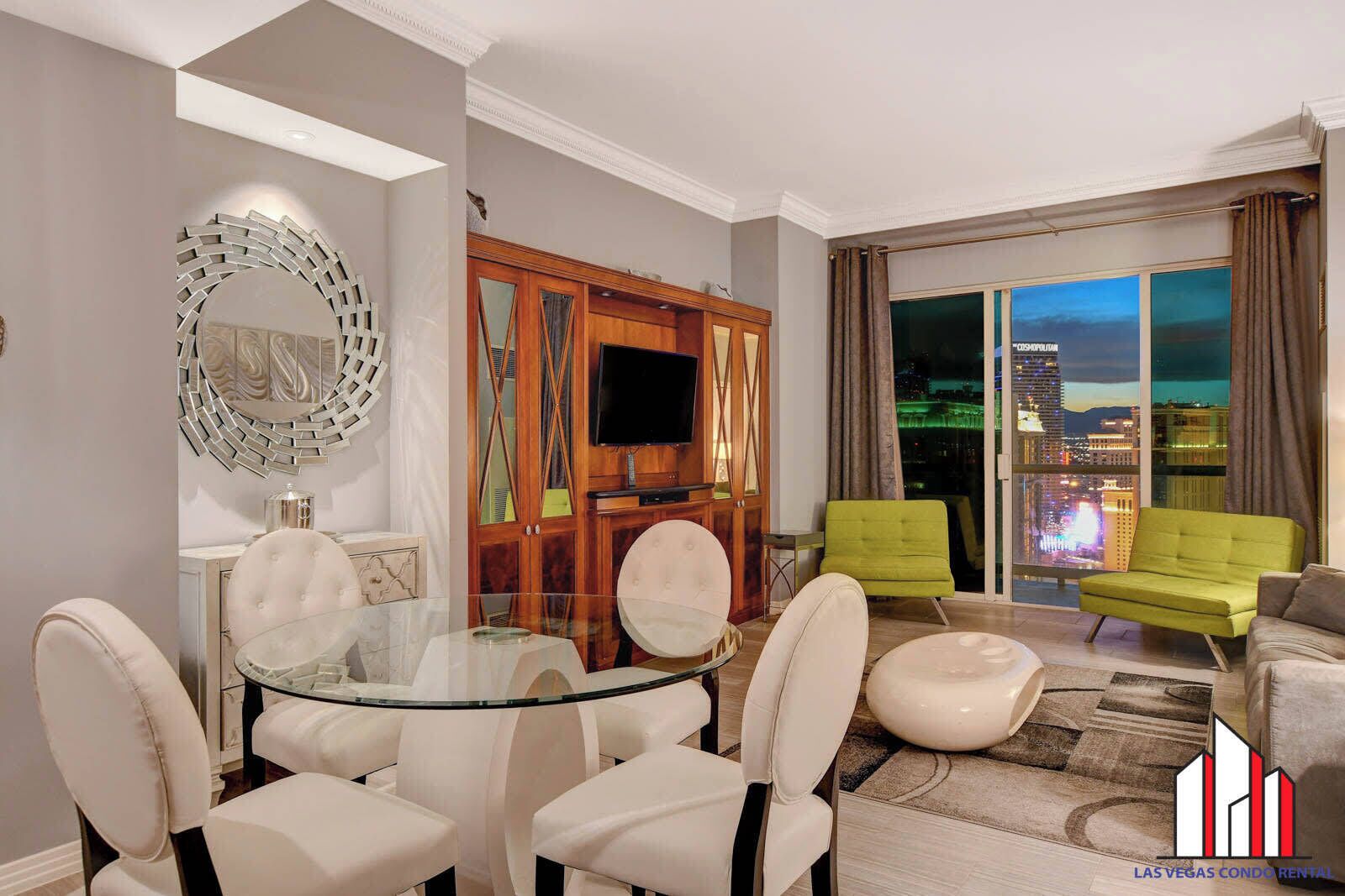 A modern living room with a glass dining table, comfortable seating, a TV, and a view of the cityscape.