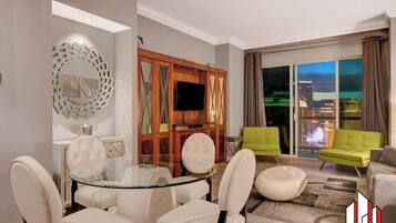 A modern living room with a glass dining table, comfortable seating, a TV, and a view of the cityscape.