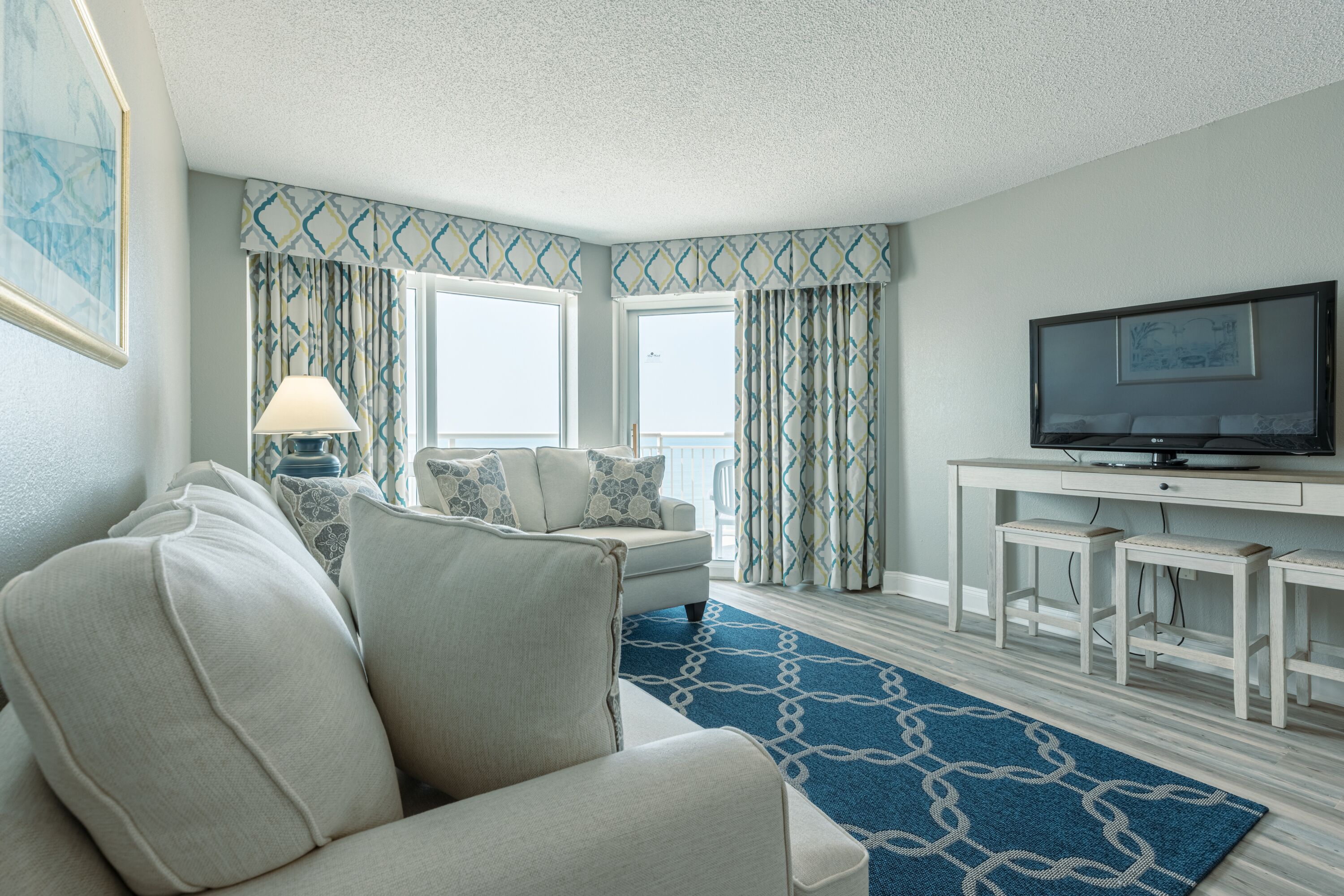 A hotel room with a sofa, a TV, a desk, and a patterned rug.
