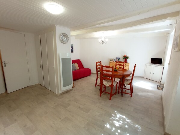 A room with a dining table, chairs, a red sofa, a TV, and a cabinet.