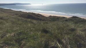 Eine Küstenlandschaft mit grüner Böschung, die zu einem Strand und dem Meer hinabführt.