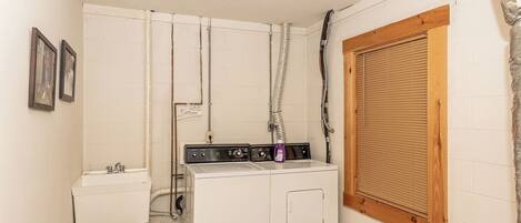 A laundry room with a washing machine, a sink, and a window with blinds.