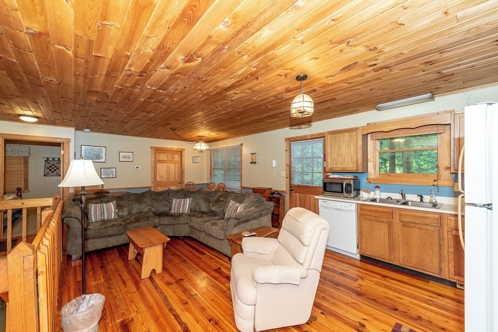 Un intérieur de chalet chaleureux avec un plafond en bois, un canapé d’angle, un fauteuil inclinable, une table à manger et un coin cuisine doté de meubles en bois et d’un four à micro-ondes.