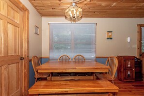 A dining area with a wooden table and chairs, a chandelier, a window with blinds, a clock, and a telephone on the wall. - This rustic home is secluded  and offers a hot-tub and wood burning fire-place (Townsend)
