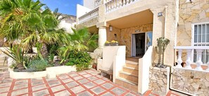 Un hôtel doté d’une façade en pierre, d’une entrée accueillante et d’un patio carrelé agrémenté de palmiers et de plantes en pot.