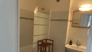 Une salle de bain avec une douche à parois de verre, une étagère en bois et un lavabo avec un miroir au-dessus.