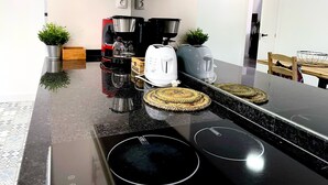 A modern kitchen with a black countertop, a coffee maker, a toaster, and a kettle. There are two potted plants and a wooden box on the counter.
