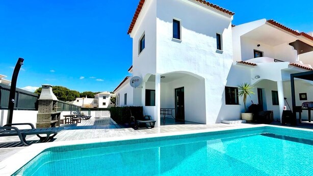 A modern two-story house with a swimming pool, outdoor furniture, and a clear blue sky.