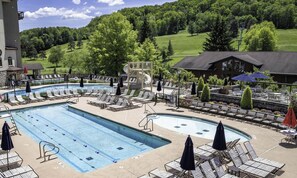 Un espace piscine avec des chaises longues, un toboggan et une vue sur un paysage verdoyant.