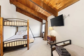 Quarto com cama de solteiro, escrivaninha com luminária, televisão na parede e janela com cortinas.