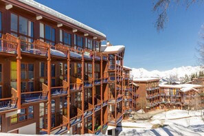 Ein mehrstöckiges Hotel mit Balkonen und großen Fenstern, umgeben von schneebedeckten Bergen.