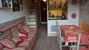 En kompakt opholdsstue med sofa, spisebord og tekøkken.