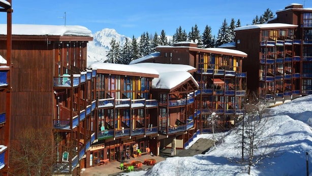 Et hotel med flere etager, altaner og et skiområde i baggrunden.