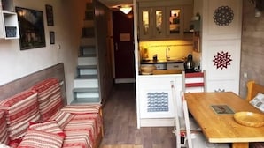 En kompakt opholdsstue med sofa, et træspisebord og et tekøkken med skabe og komfur.