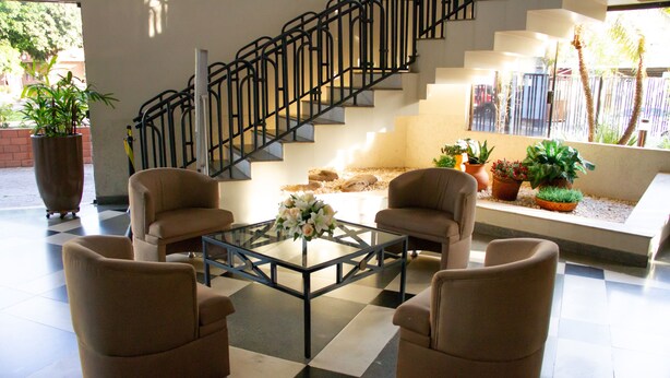 Un vestíbulo con piso a cuadros, una mesa de centro de vidrio, cuatro sillones, una escalera y plantas en macetas.