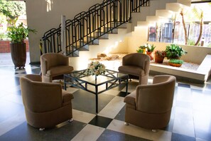 Eine Lobby mit Schachbrettfußboden, einem Glastisch, vier Sesseln, einer Treppe und Topfpflanzen.
