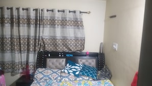 Un dormitorio con cama, cortinas estampadas, mesita de noche y lámpara de pared.