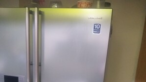 Un refrigerador de acero inoxidable con pantalla digital, compartimento congelador y etiqueta de garantía de 10 años.