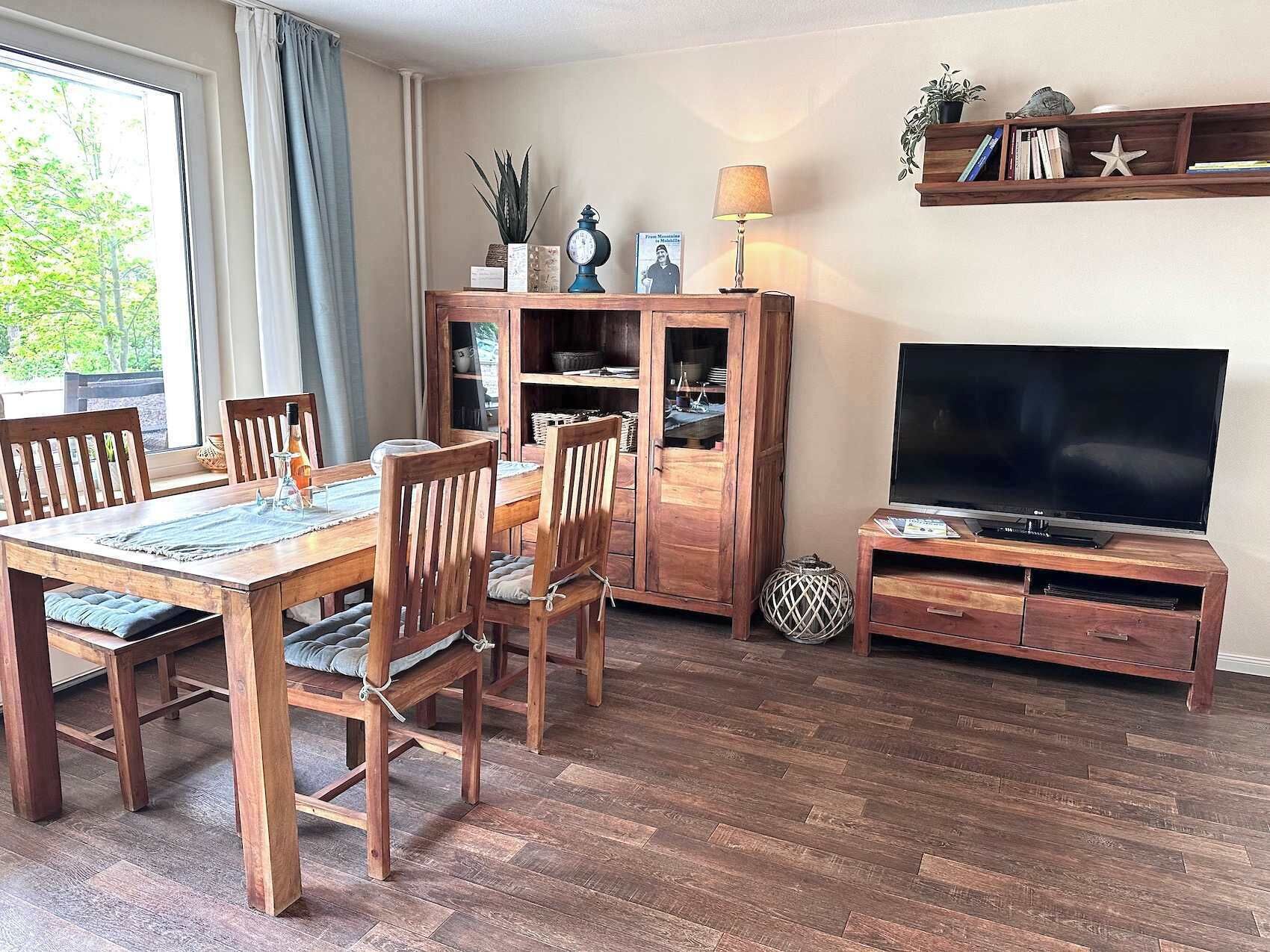 Ein Essbereich mit Holztisch und -stühlen, einer Vitrine, einem Fernseher auf einem Holzschrank und einem Regal mit Büchern und Dekoration.