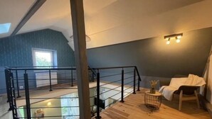 A spacious loft bedroom with a high ceiling, a wooden floor, a balcony with a black railing, and a large window providing natural light. - Juliette's garden (Gournay-le-Guérin)
