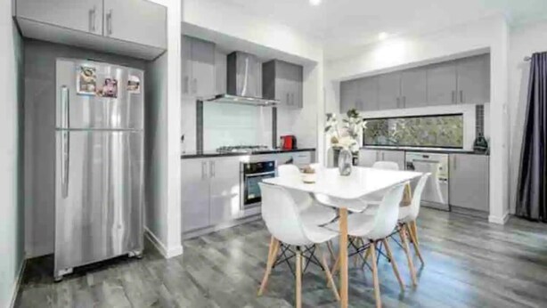 A modern kitchen with grey cabinets, a stainless steel refrigerator, and a dining area with a white table and chairs. - ADORABLE 2 Bedroom + Study Villa - free parking. (Rosebud)