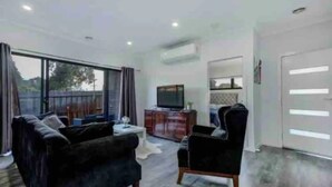 A living room with a sofa, armchair, TV, and a small table. - ADORABLE 2 Bedroom + Study Villa - free parking. (Rosebud)