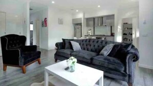 A modern living room with a dark grey sofa, a black armchair, and a white coffee table. - ADORABLE 2 Bedroom + Study Villa - free parking. (Rosebud)
