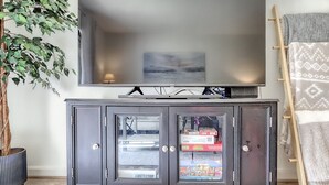 Een woonkamer met een flatscreen televisie aan de muur, een donkere houten kast met glazen deuren, een potplant en een houten ladder die tegen de muur staat.