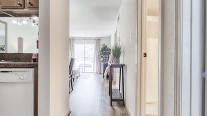 Een ruime hal met houten vloeren, een keuken aan de linkerkant, en een eethoek met een tafel en stoelen.